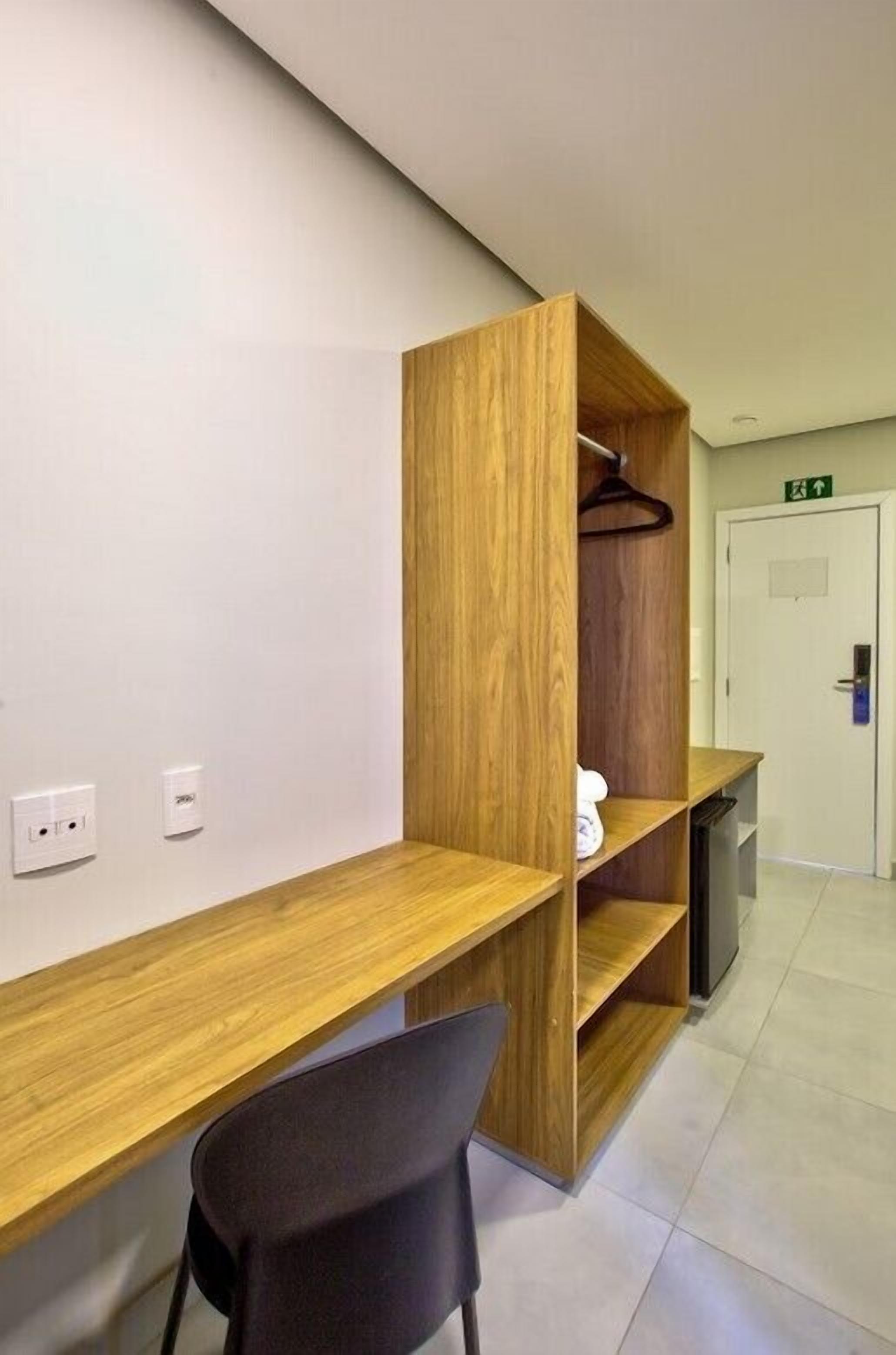 Una habitación de hotel moderna con un escritorio de madera, una silla negra y un armario con perchero.