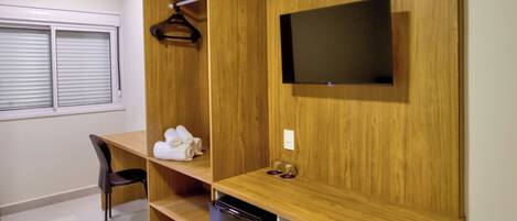A compact room with a wooden desk, a TV mounted on the wall, a small seating area, and a built-in dishwasher.