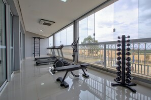 Une salle de sport équipée de matériel d’exercice, dotée de grandes fenêtres et offrant une vue sur l’extérieur.