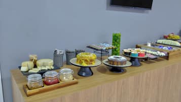 Mostrador de buffet con diversas opciones de comida, incluyendo quesos, pasteles y frutas.