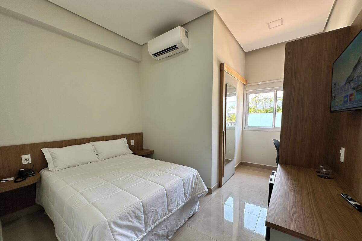A hotel room with a bed, bedside table, and a TV on a wooden stand.