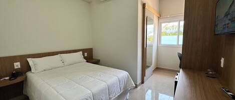 A hotel room with a bed, bedside table, and a TV on a wooden stand.