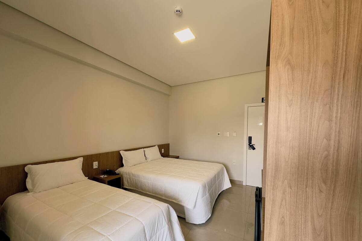 A hotel room with two beds, a wooden headboard, a bedside table with a phone, and a door with a handle.