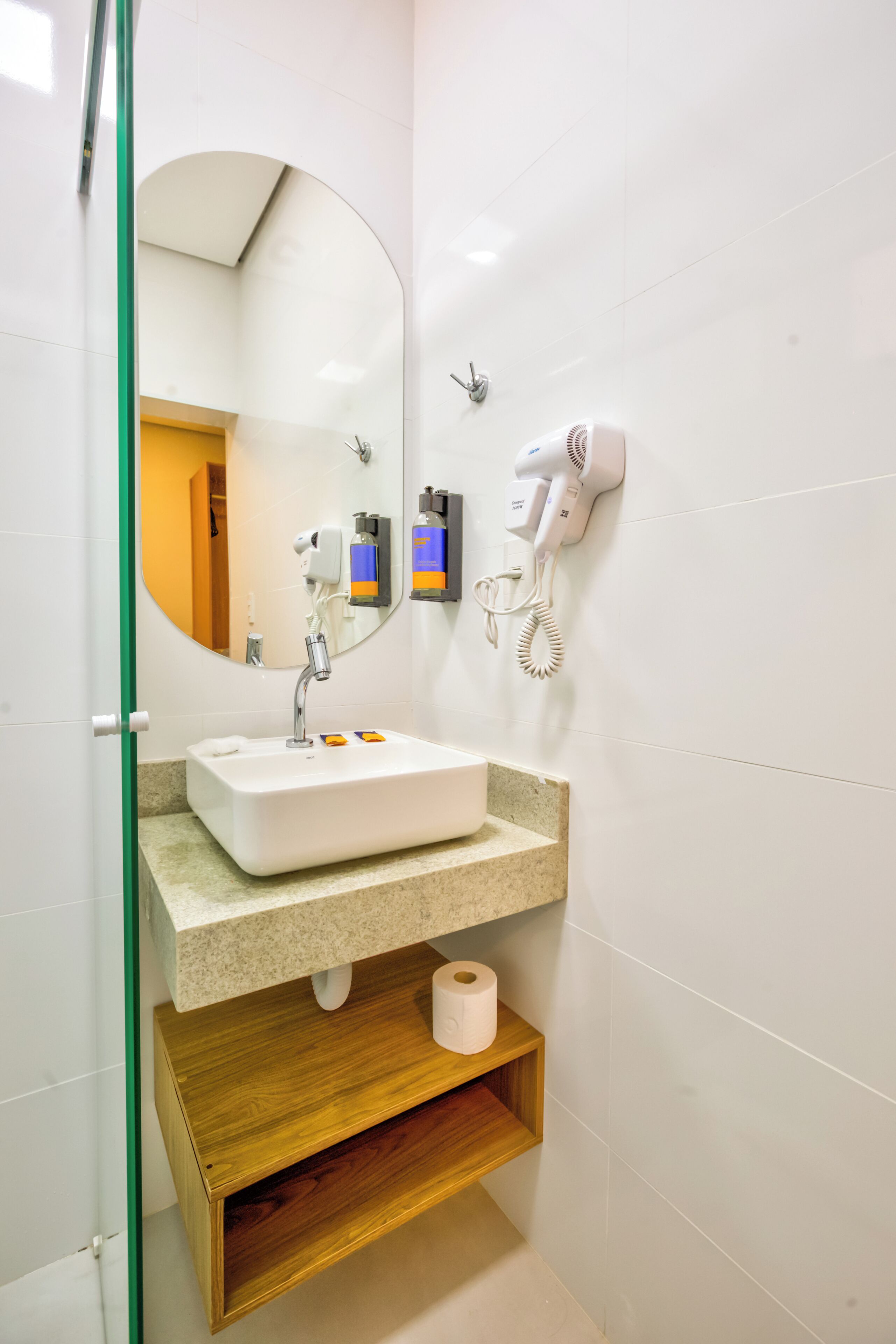 A bathroom with a white sink, a mirror, a hairdryer, and a towel dispenser.