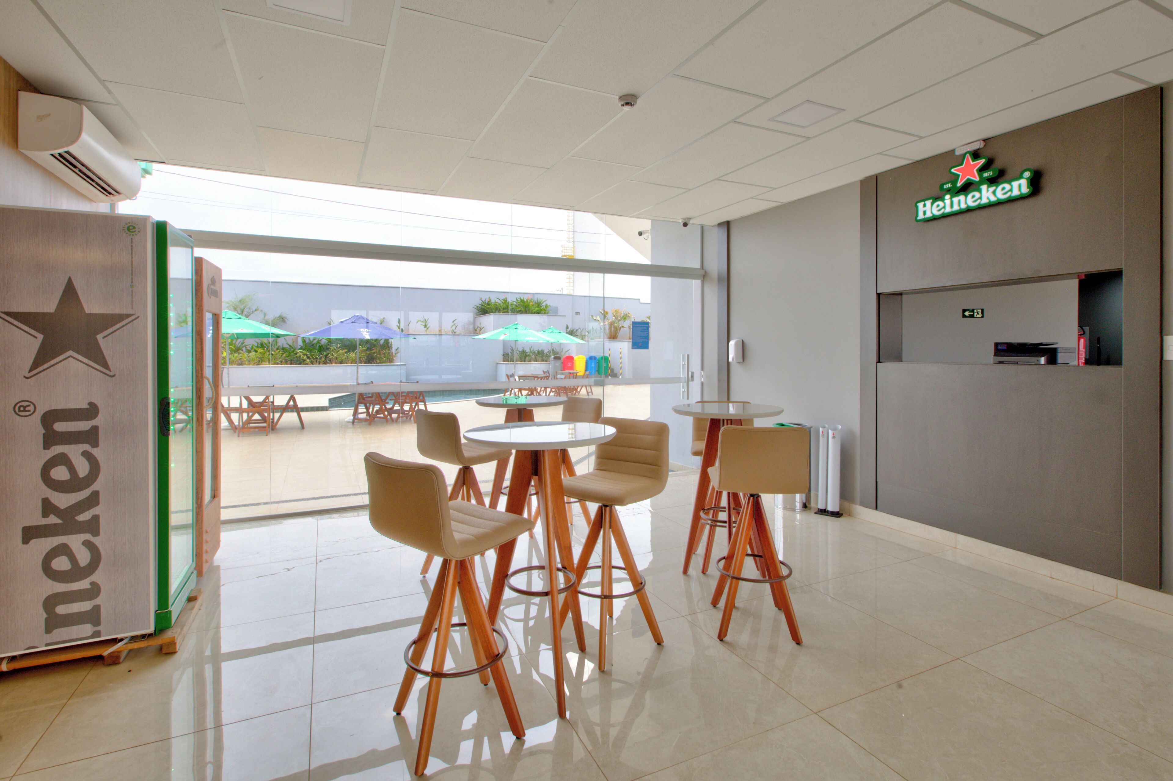 A modern interior with a Heineken sign, a glass door leading outside, and several tables and chairs.