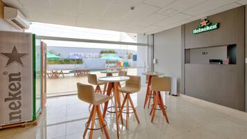 Un interior moderno con un letrero de Heineken, una puerta de vidrio que da al exterior y varias mesas y sillas.