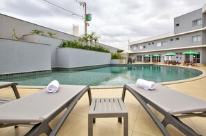 A swimming pool with lounge chairs and umbrellas, surrounded by a building with a tiled exterior. - Comfort Serra da Canastra  (São João Batista do Glória)