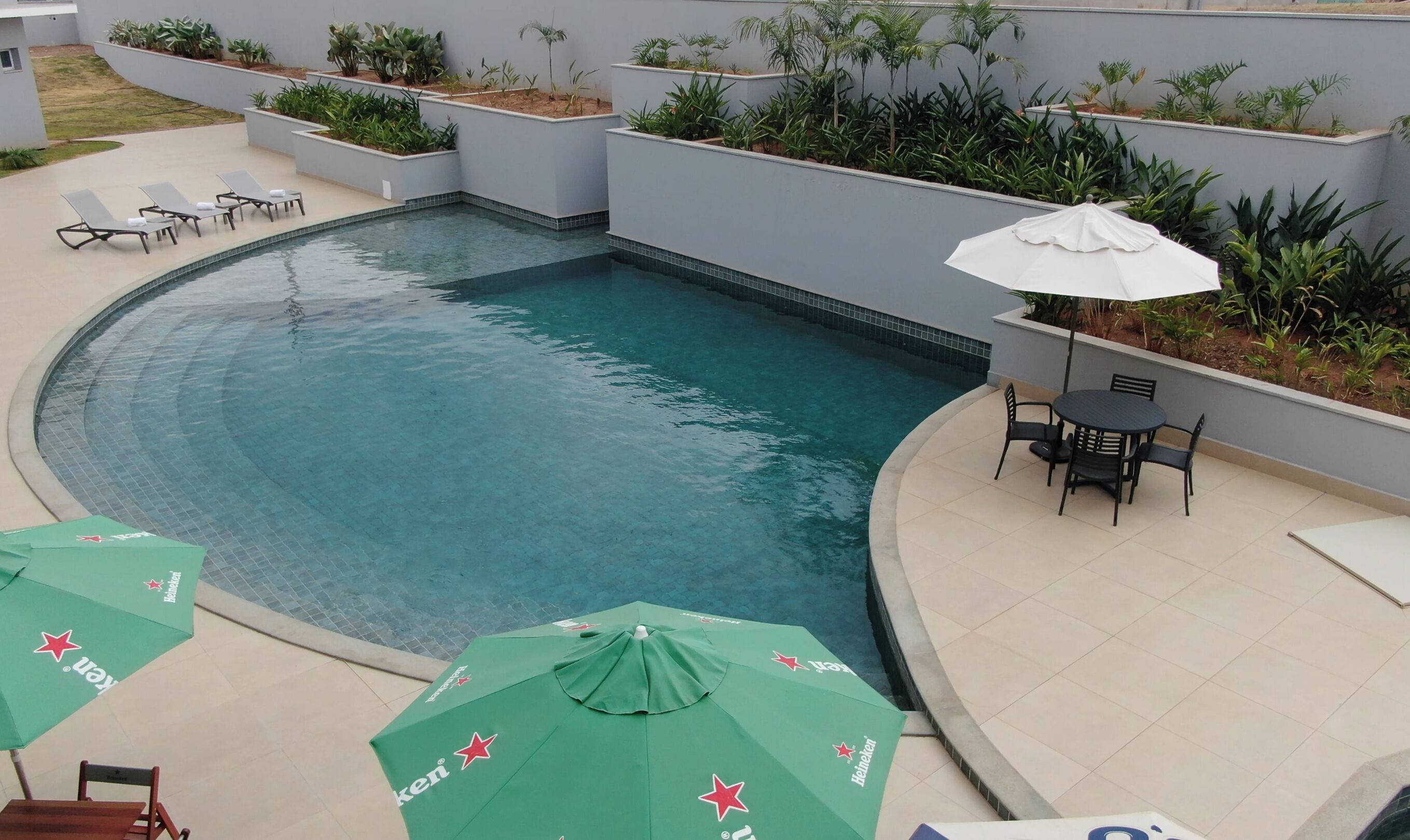 A swimming pool with lounge chairs and umbrellas, surrounded by planters and a tiled patio area.