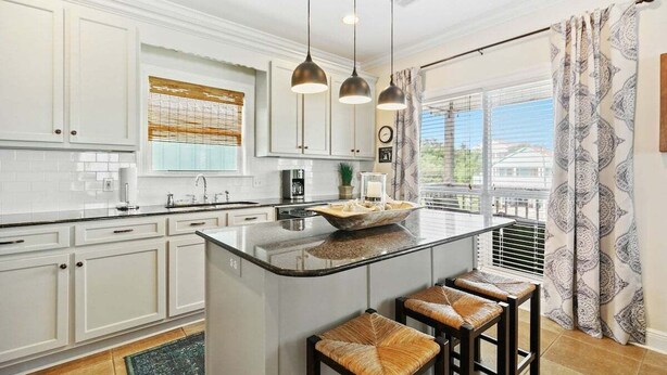 A kitchen with white cabinets, a large island with stools, pendant lighting, and a view through the window. - Bear Point 3BR House Orange Beach Bring Your Boat! (Orange Beach)