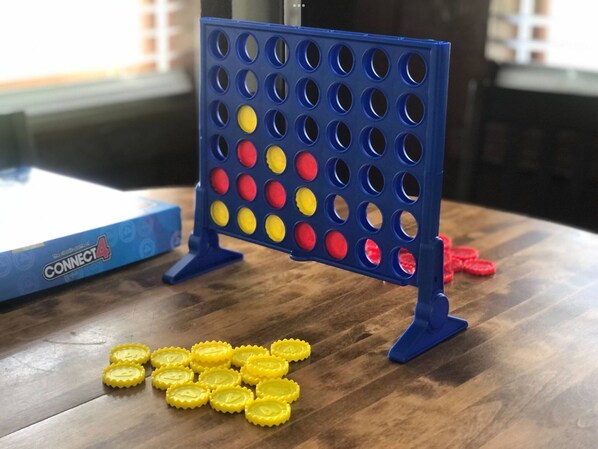 Et Connect4 spilbræt med en blå holder, gule og røde spillebrikker, og en Connect4 æske på et træbord.