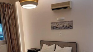 A hotel room with a bed, a nightstand, an air conditioning unit, a painting, and a window with curtains. - Athenian Center Athens Kolonaki (Athina)