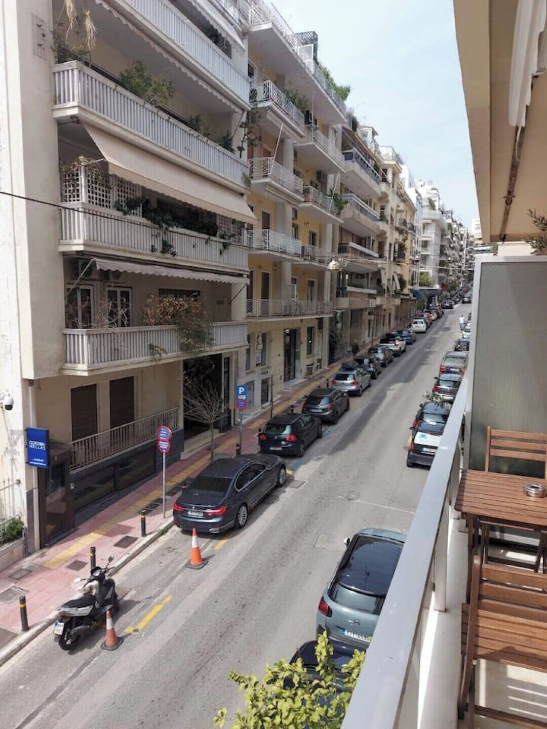 A multi-story residential building with balconies, parked cars, and a pedestrian walkway.