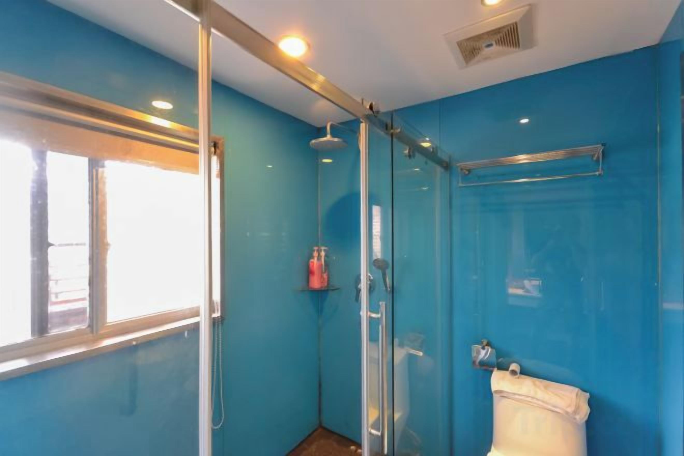 A bathroom with a glass shower enclosure, a toilet, and a window providing natural light.