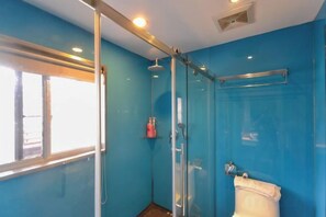 A bathroom with a glass shower enclosure, a toilet, and a window providing natural light. - Pugongying Hotel (Yuhuan)