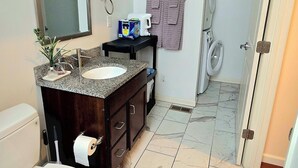 Casa de banho com sanita, lavatório, espelho, porta-toalhas e chuveiro.