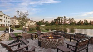 An outdoor patio area with a brick fire pit, Adirondack chairs, and a view of a lake.