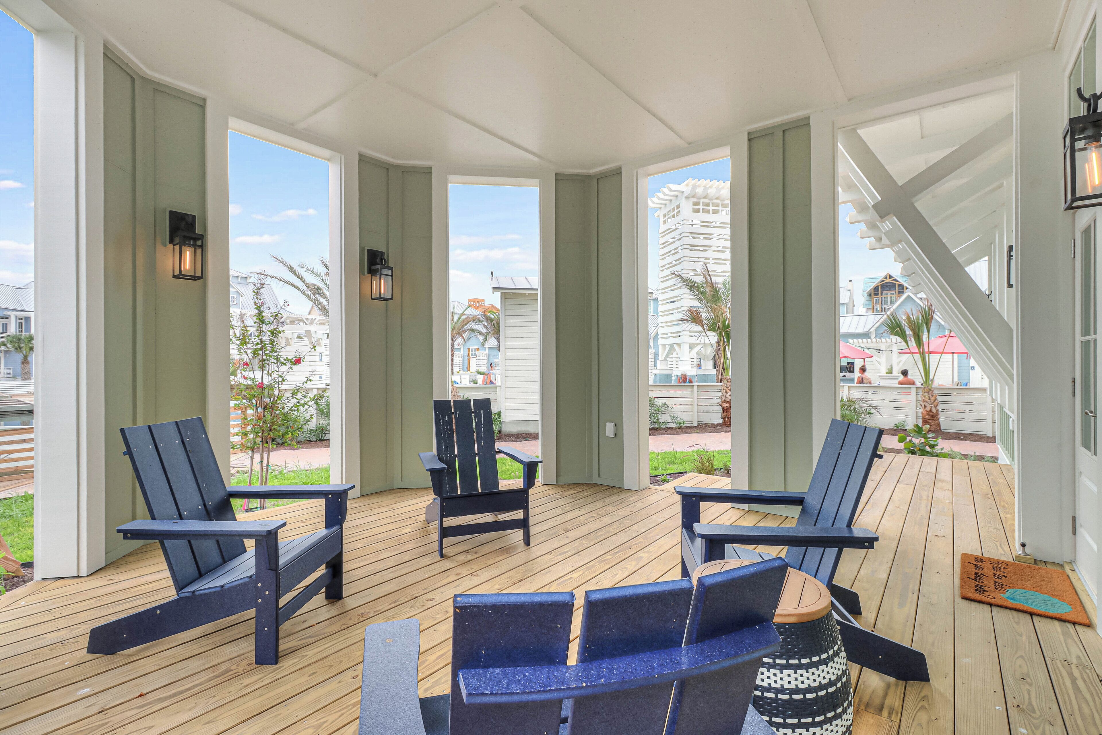 A covered outdoor seating area with Adirondack chairs and a bench, overlooking a view of buildings and a palm tree.