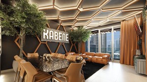 A modern dining area with a geometric wall design, a large chandelier, and a view of the city through floor-to-ceiling windows.