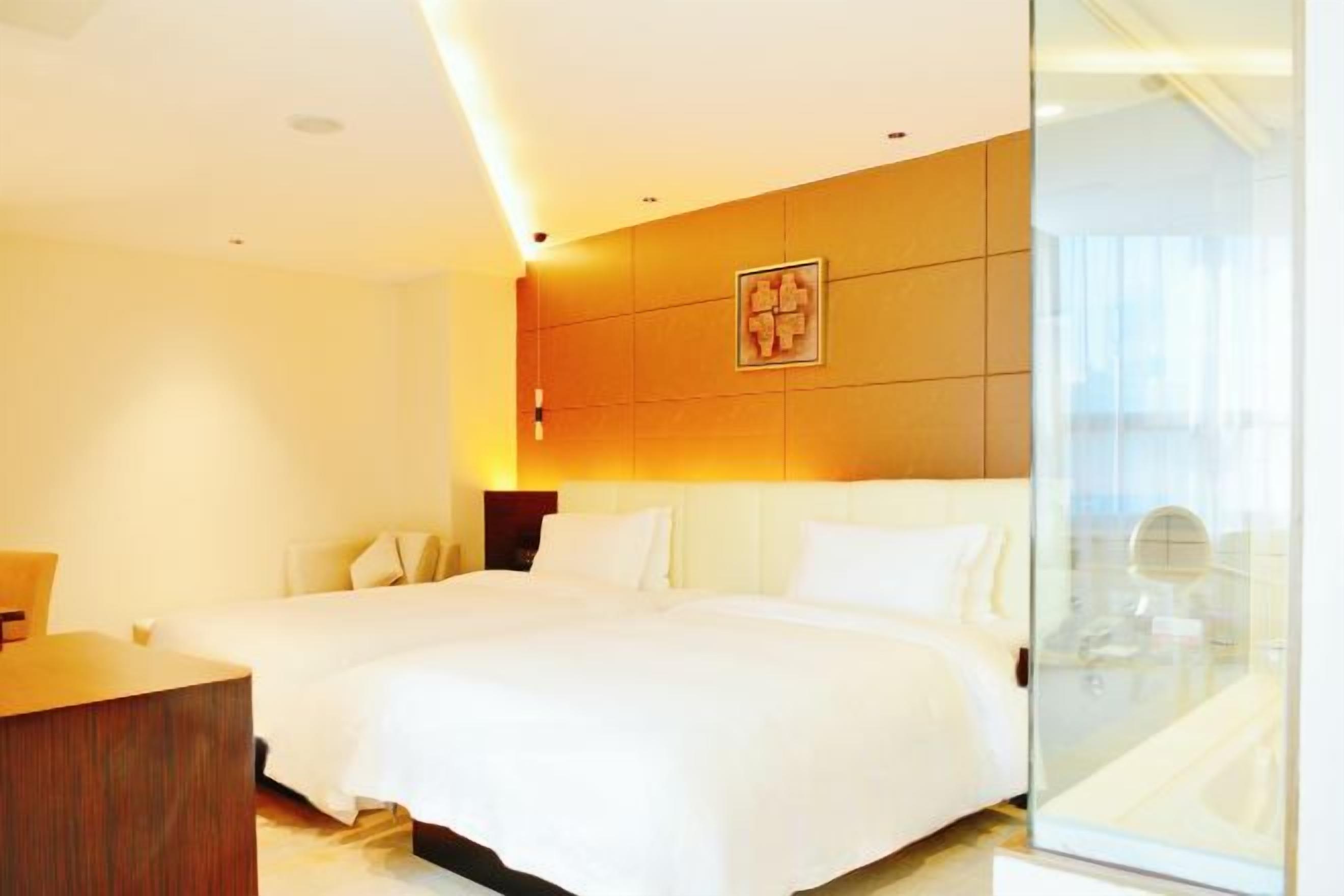 A hotel room with a large bed, a bedside table, and a glass partition wall.