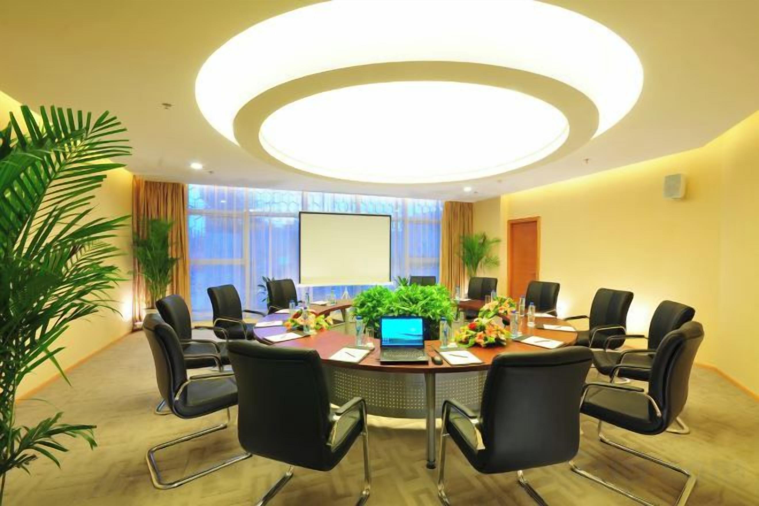 A conference room with a round table, black chairs, a laptop, and a projector screen.