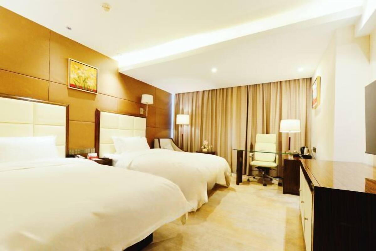 A hotel room with two beds, a desk, a chair, and a television.