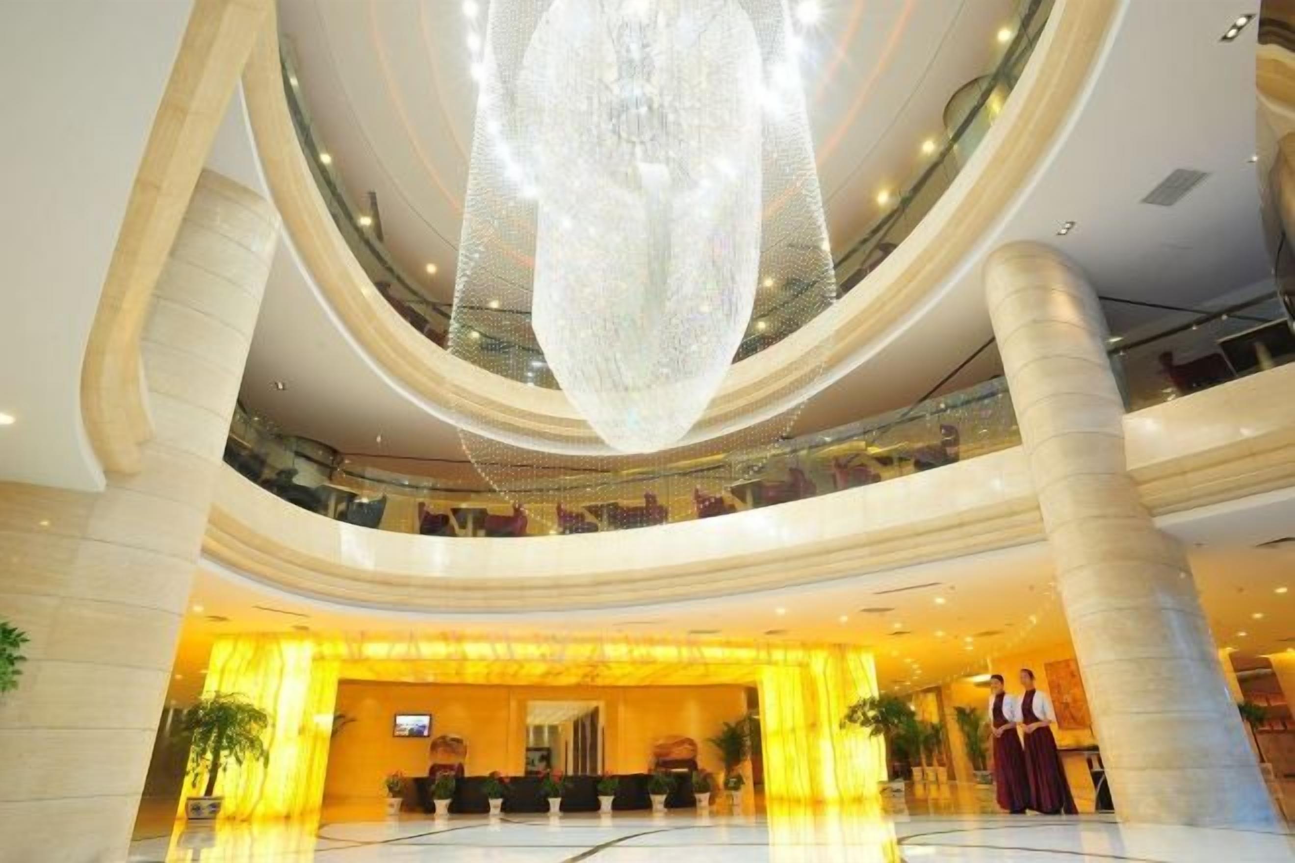 A multi-level hotel lobby with a large chandelier, a reception desk, and a seating area.