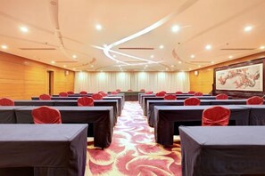 Un salón de conferencias con filas de mesas, un escenario y una pantalla grande.