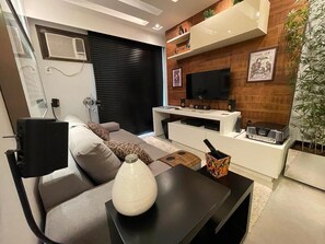 A modern living room with a sofa, a coffee table, a TV, and a wooden wall panel. - Ap em Niterói com Varanda e Garagem (Niteroi)