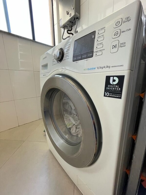 A front-loading washing machine with a digital control panel, a 10-year warranty badge, and a window above it. - Ap em Niterói com Varanda e Garagem (Niteroi)