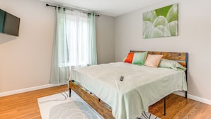 Een slaapkamer met een bed, een televisie aan de muur en een raam met gordijnen.