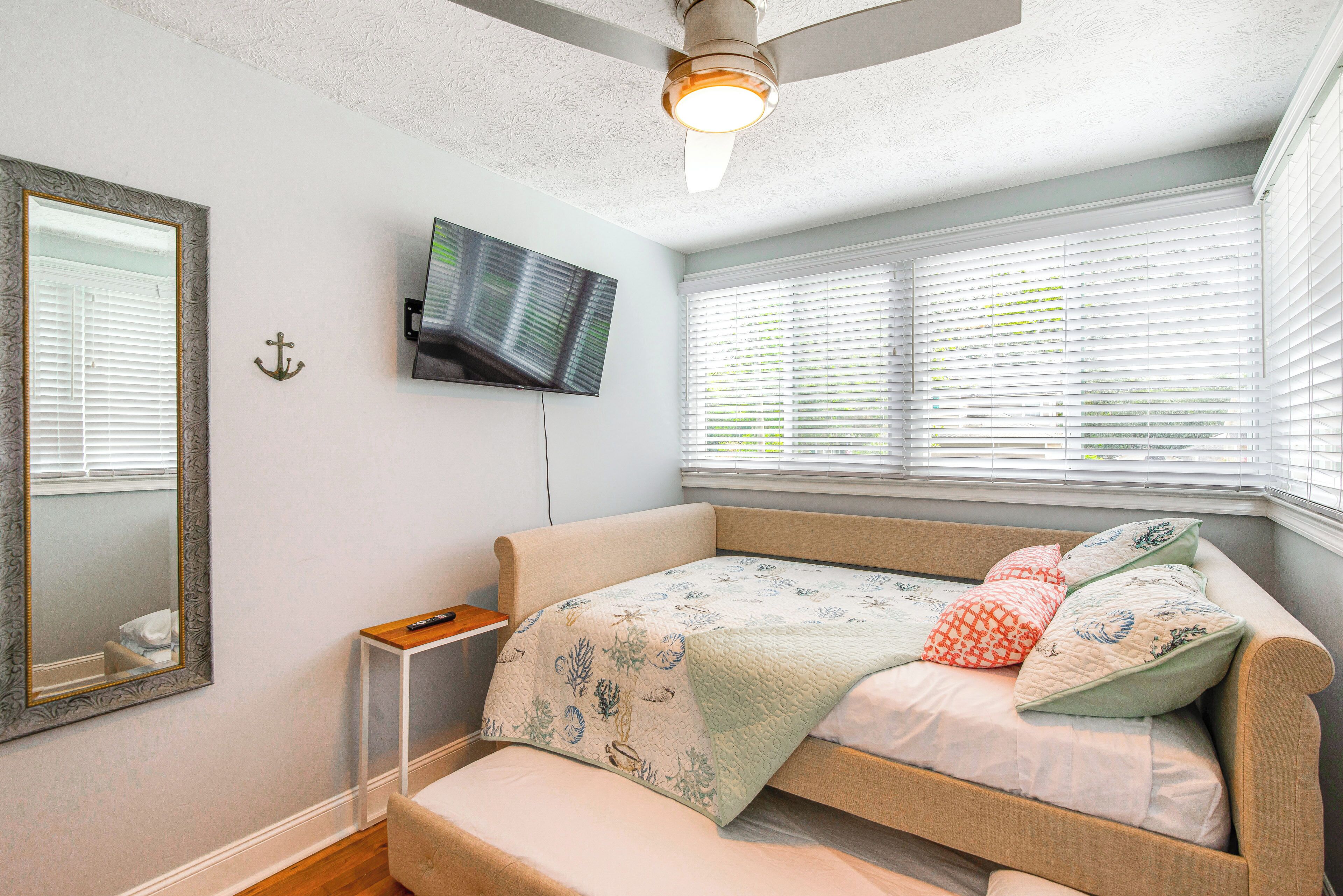 A bedroom with a bed, a TV mounted on the wall, and a window with blinds.