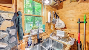 A rustic wooden cabin interior with a stone wall, wooden shelves with potted plants, a sink, and a window with a view of greenery. - Cozy Nature Escape! Roaring Gap Cabin w/ Patio (Roaring Gap)