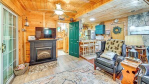 A cozy cabin interior with a fireplace, wooden walls, a dining area, and a living room with a leather sofa and a table lamp. - Cozy Nature Escape! Roaring Gap Cabin w/ Patio (Roaring Gap)