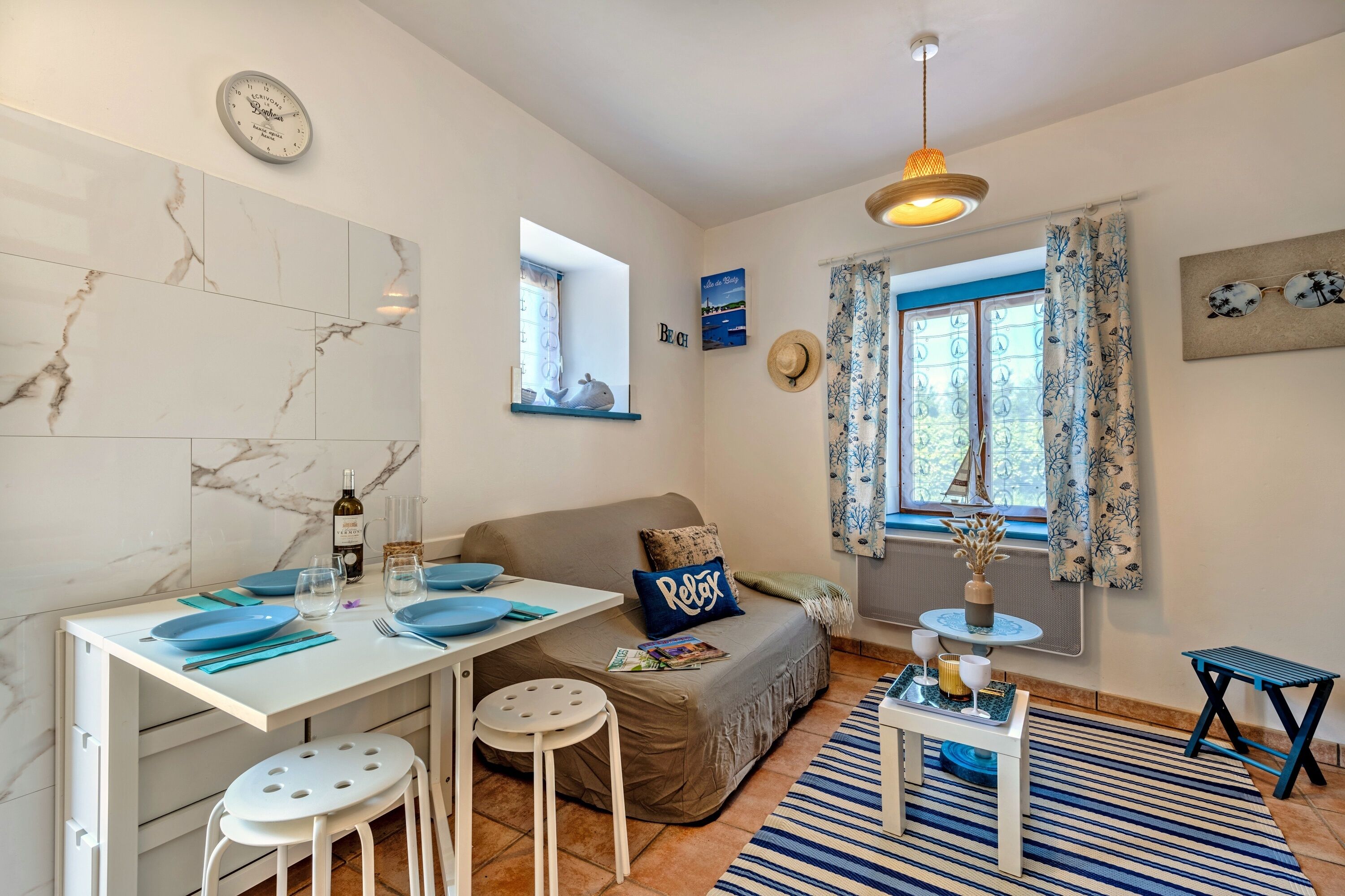 Un espace de vie compact comprenant un coin repas, un canapé, une petite table et une fenêtre avec des rideaux.