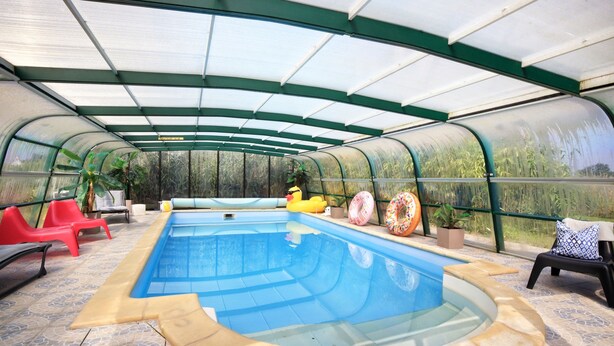 A covered swimming pool with a glass ceiling, surrounded by lounge chairs and potted plants. - La Maison Merlin - Maison avec piscine, Sénoville (Sénoville)