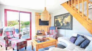 A living room with a sofa, armchairs, a coffee table, a staircase, and a large window. - La Maison Merlin - Maison avec piscine, Sénoville (Sénoville)