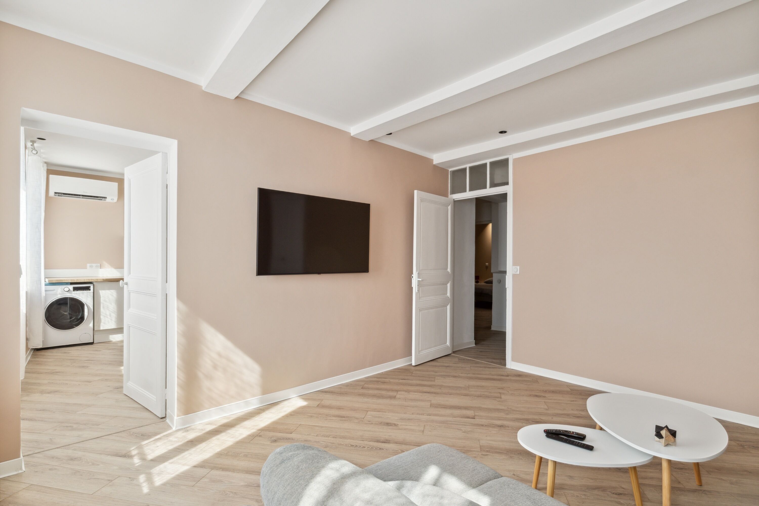 A modern living room with a sofa, a small white table, and a flat-screen TV mounted on the wall.