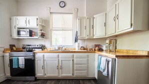 Una cucina con mobili bianchi, un forno a microonde, un piano cottura, un lavandino e una sveglia appesa al muro.