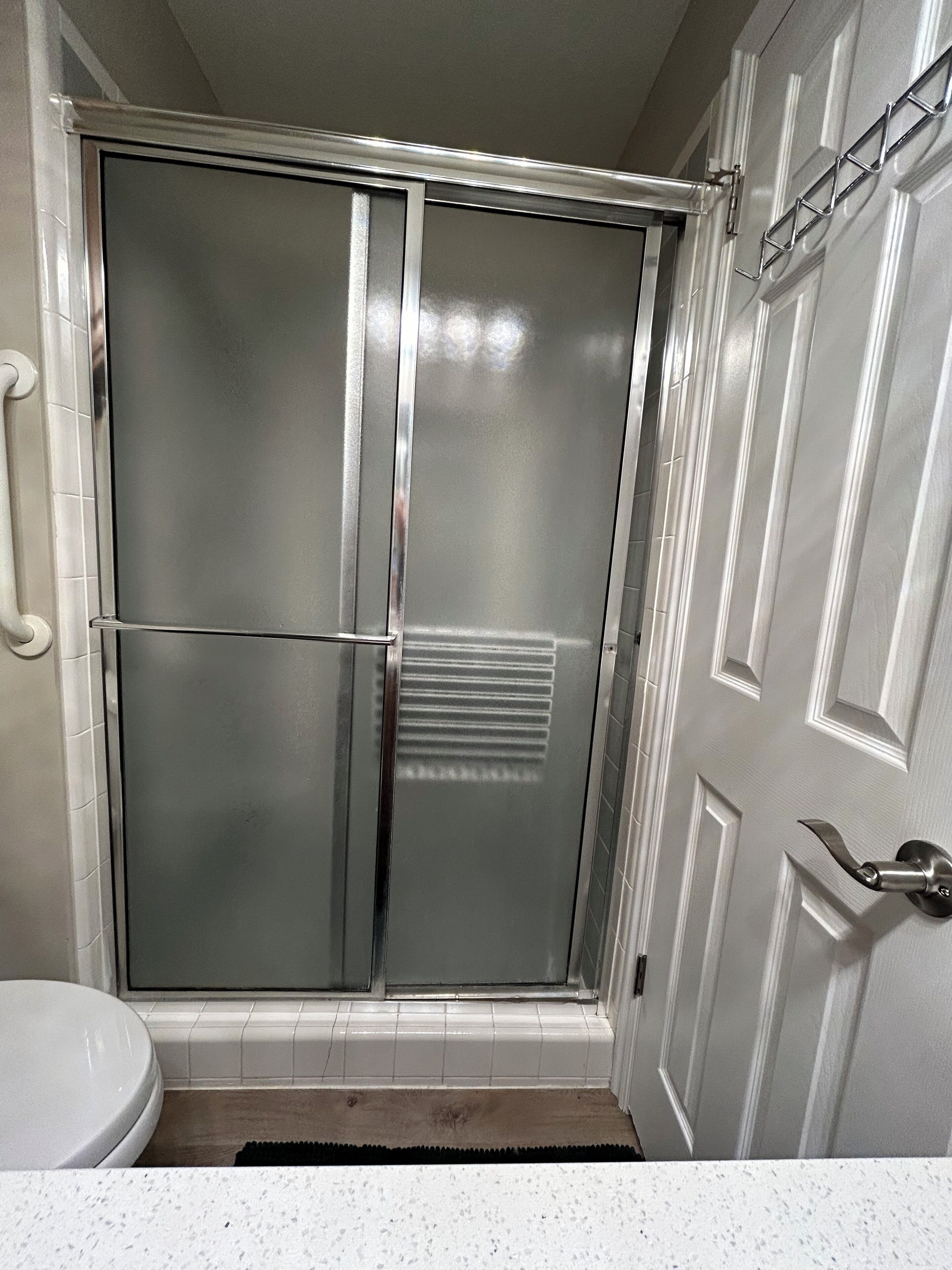 A bathroom with a shower enclosure, a toilet, and a door with a handle.
