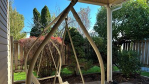 Eine überdachte Veranda mit Schaukelstuhl, Holzlattenzaun und verschiedenen Bäumen und Sträuchern.