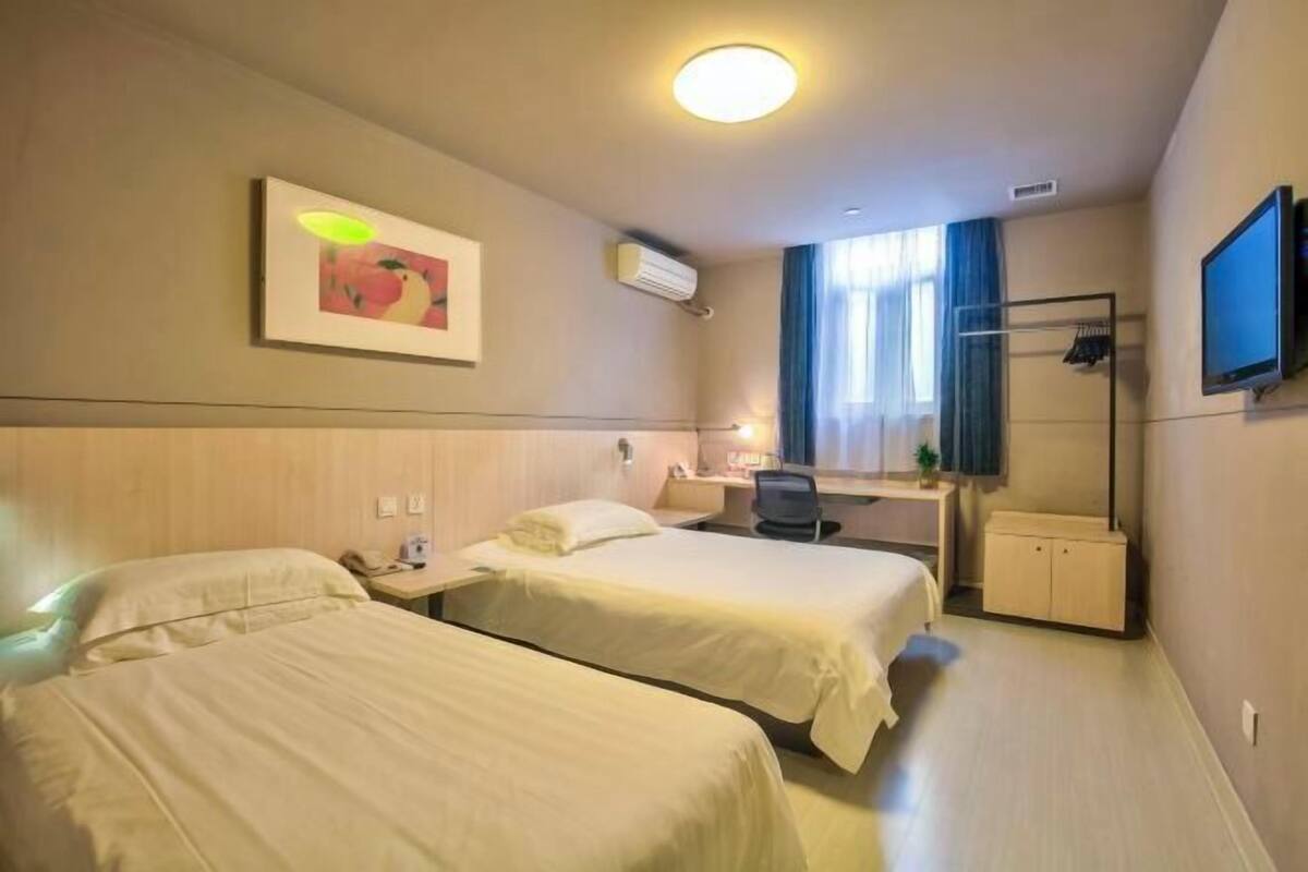 A hotel room with two beds, a desk, a chair, a TV, and a window with curtains.