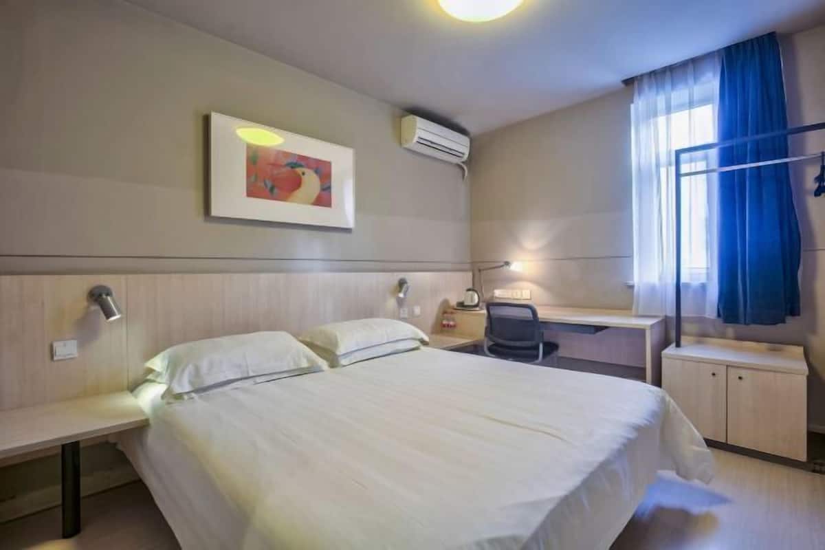 A hotel room with a bed, desk, chair, and a window with curtains.