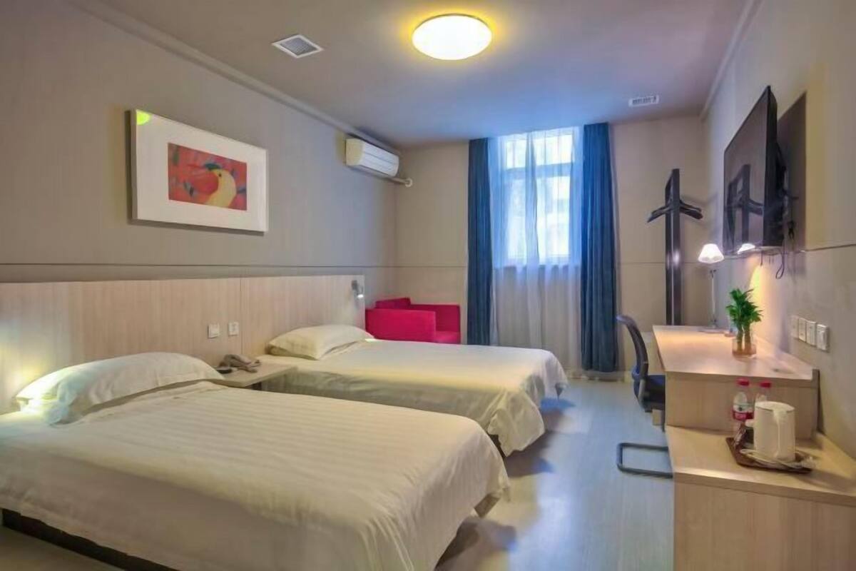 A hotel room with two beds, a desk, a chair, a TV, and a window with curtains.