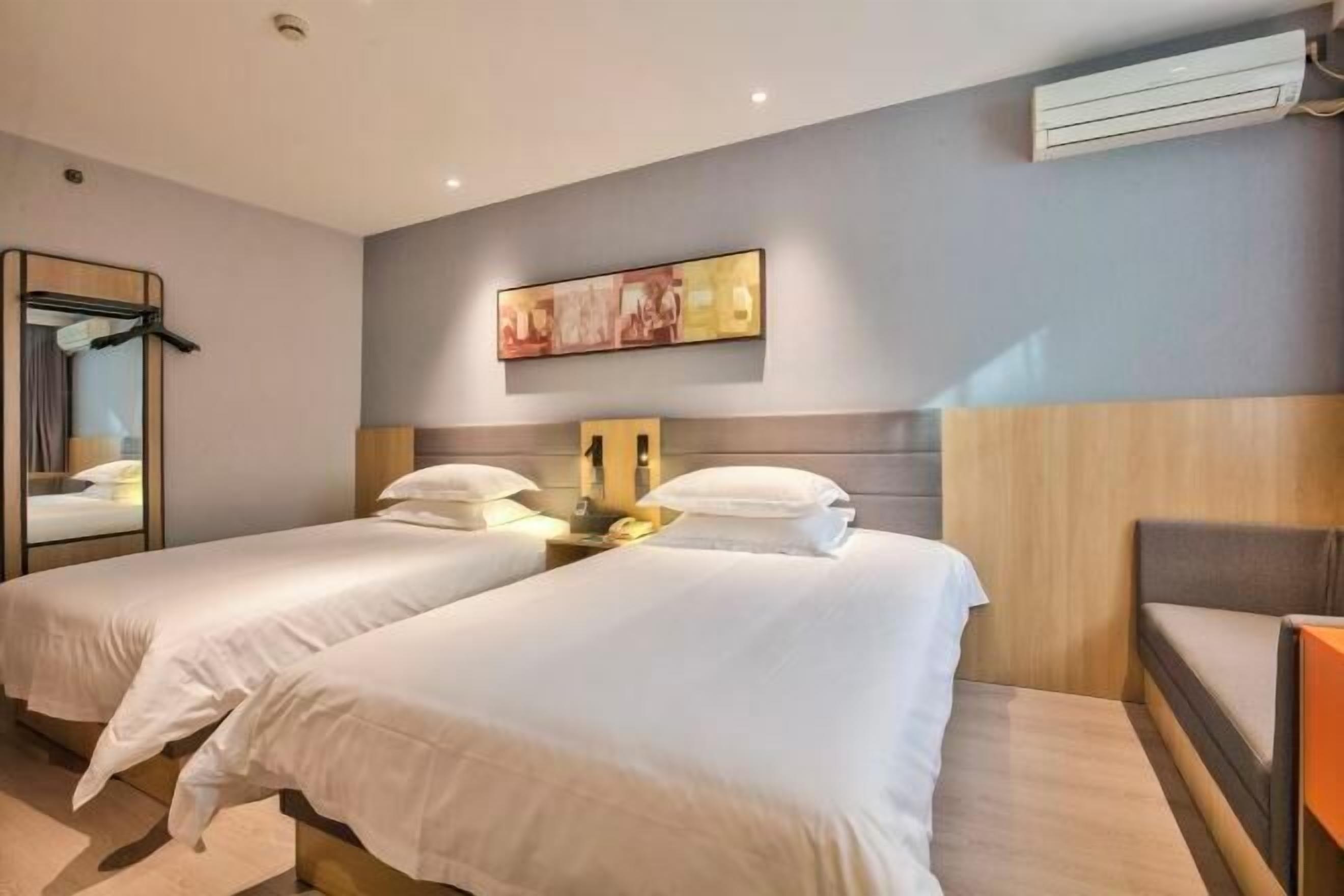 Una habitación de hotel con dos camas, un espejo, un cuadro y un equipo de aire acondicionado.