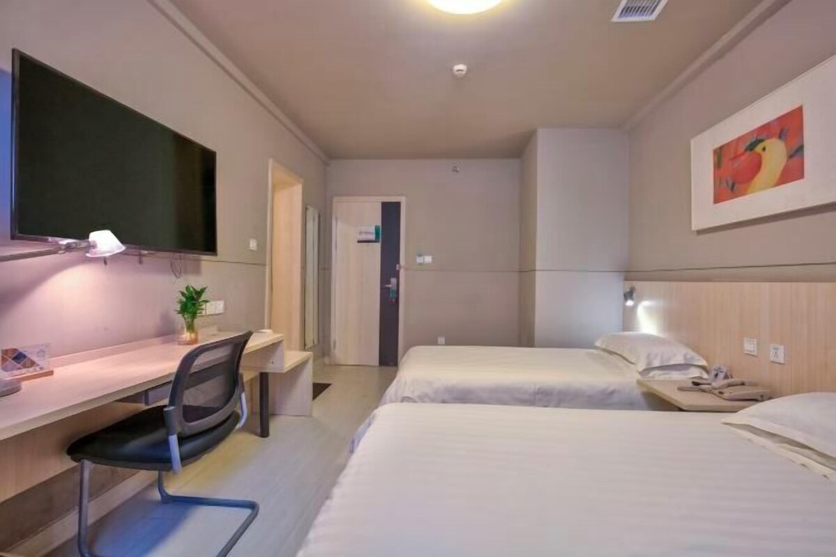A hotel room with a desk, two beds, a TV, and a painting.