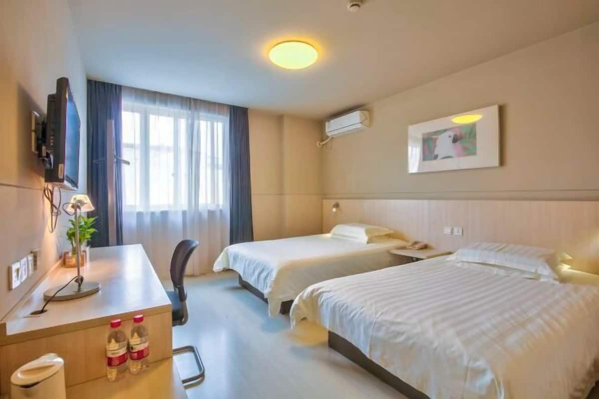 A hotel room with two beds, a desk with a lamp, a TV, and a window with curtains.
