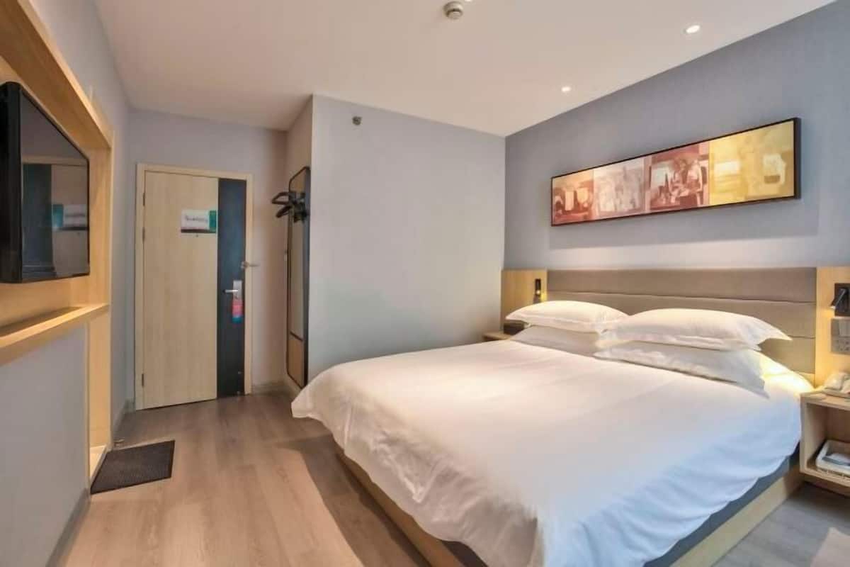 A hotel room with a bed, a door, a wall-mounted artwork, and a bedside table.