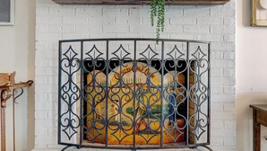 Een open haard met een bakstenen omlijsting, een decoratief metalen rooster en een plank met een plant.