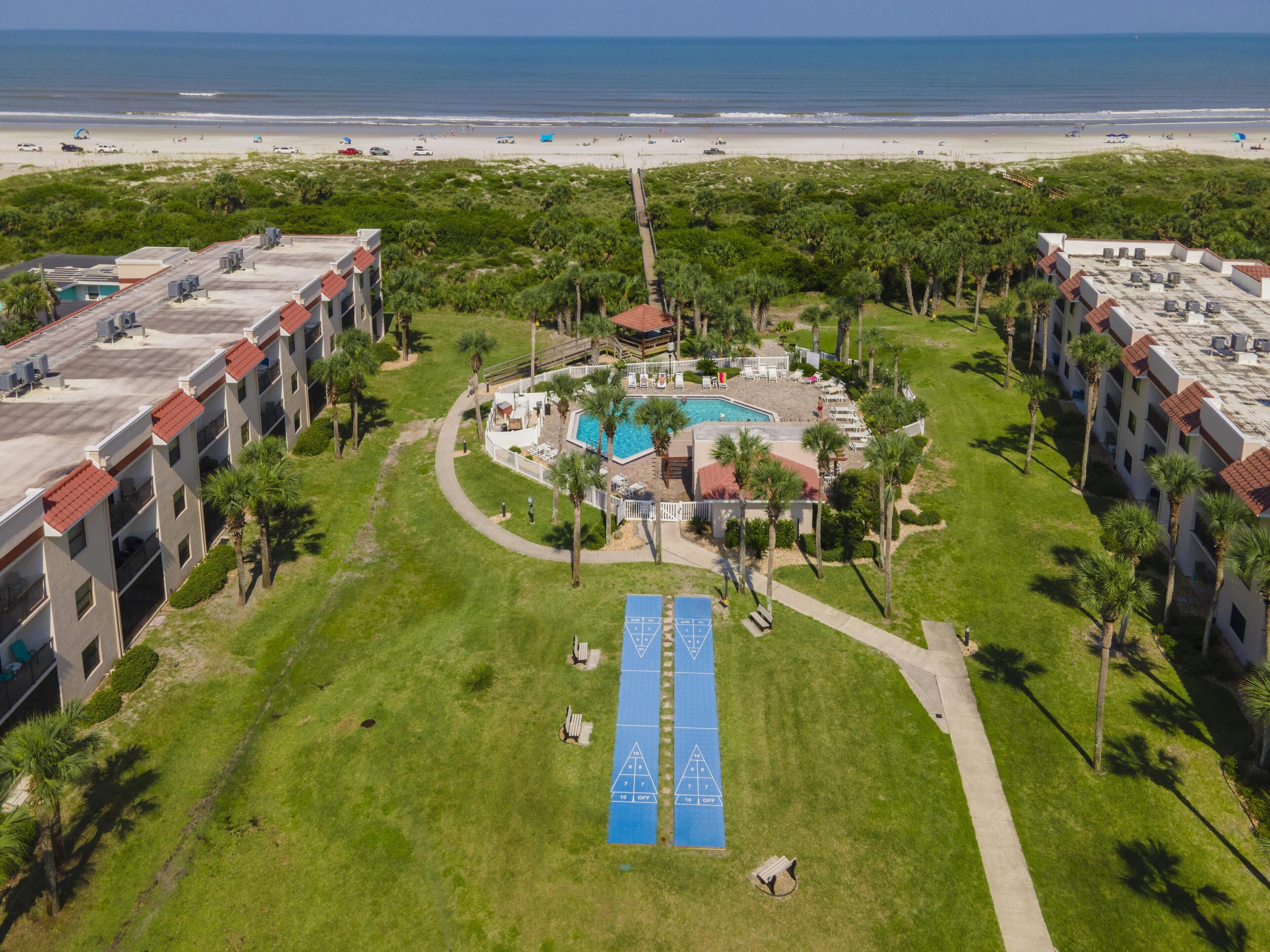 Vista aérea de un hotel con piscina, cancha de tenis y acceso a la playa.