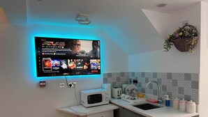 A modern kitchen with a flat-screen TV mounted above the counter, a microwave, and a sink with a tiled backsplash. - Central Luton Executive Suite (Luton)